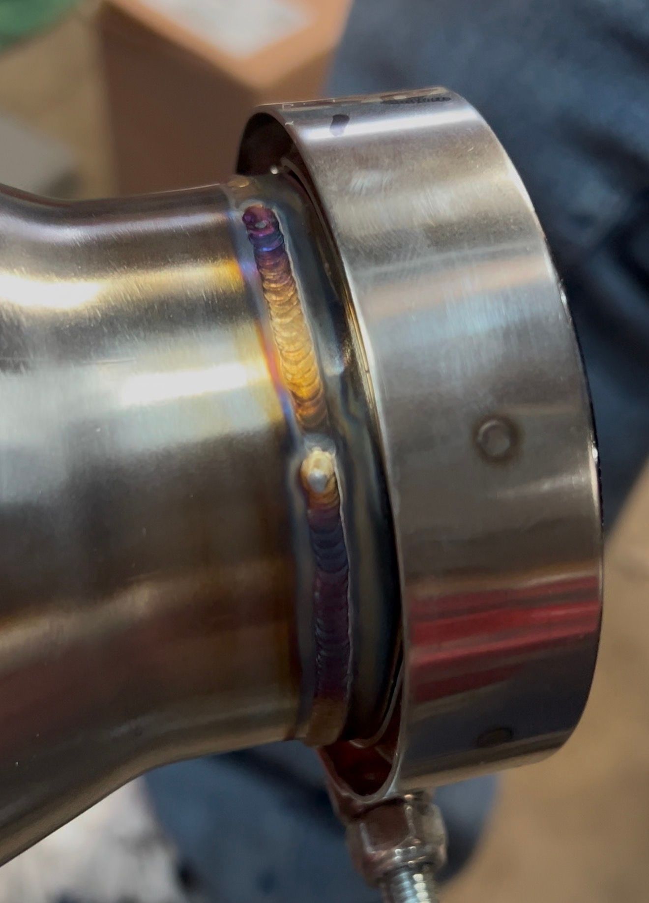 Close-up of a V-band flange TIG-welded to stainless pipe with heat tint around the bead.