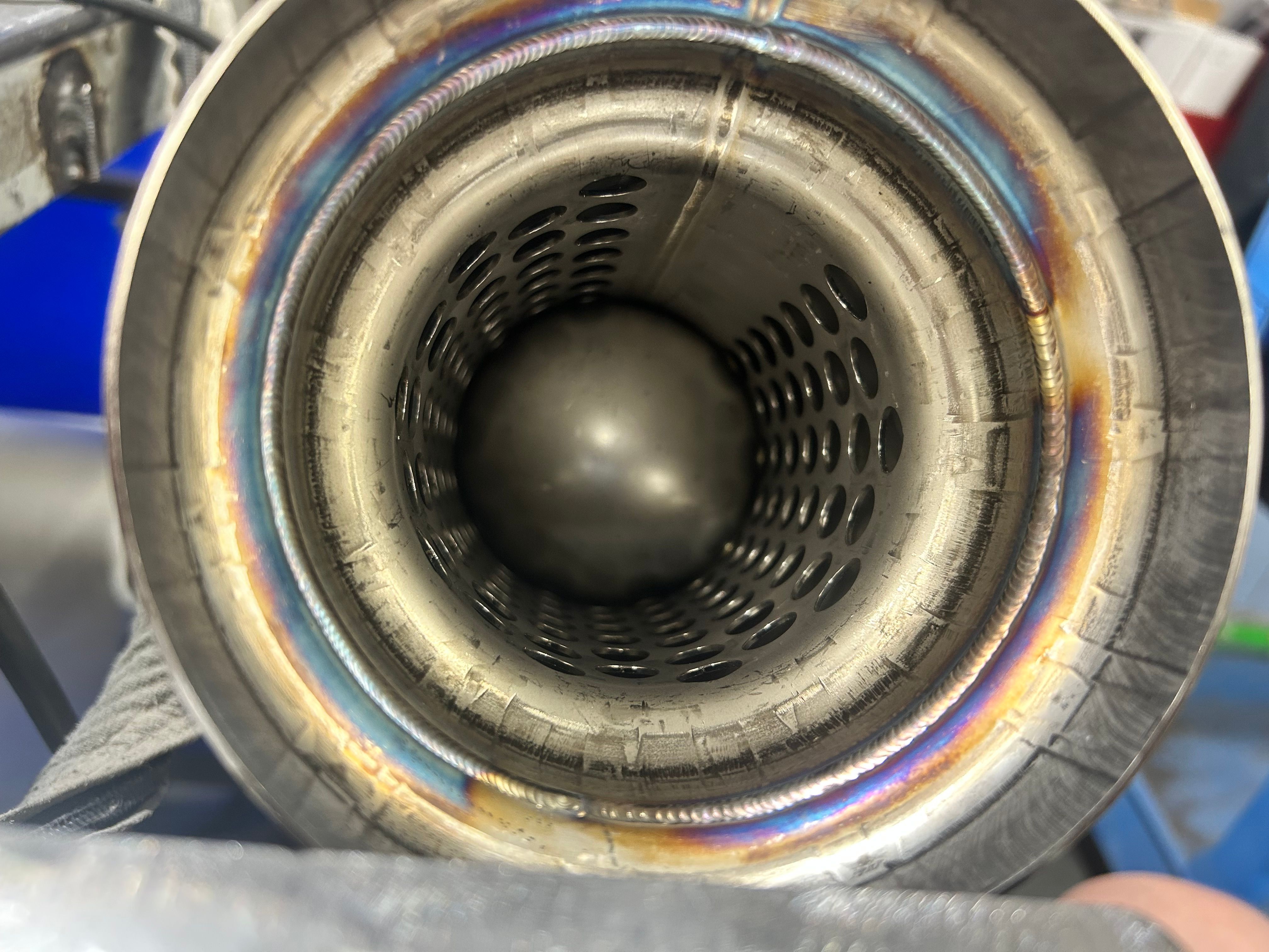 Looking down the bore of a stainless resonator: a full ring of weld with heat tint around a perforated core.